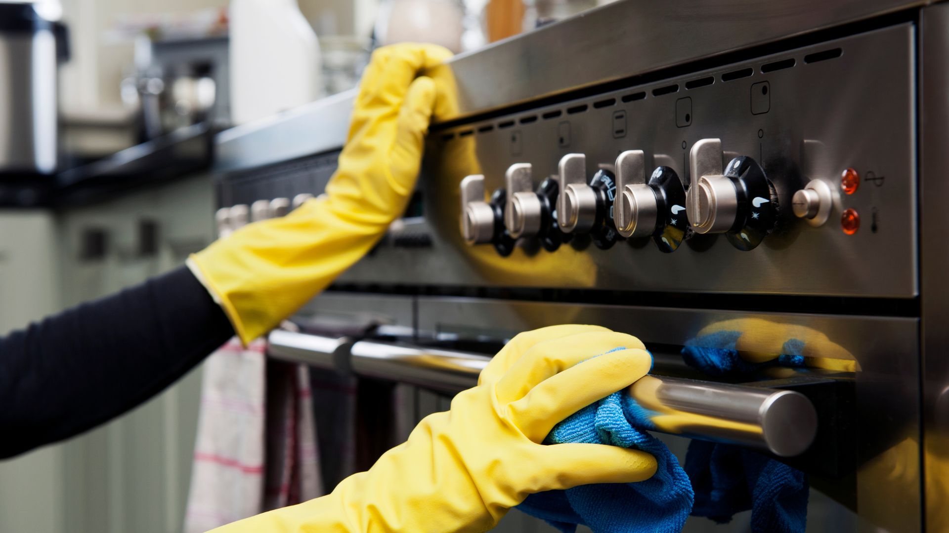 A person cleaning a stove with a yellow glove